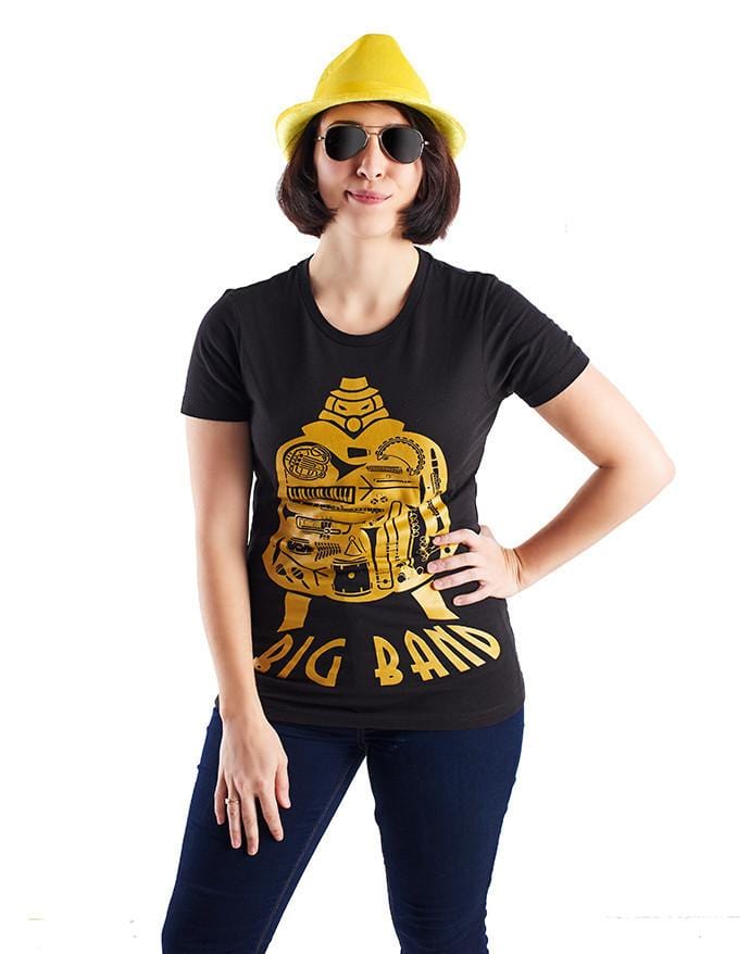 Image of the Big Band shirt, which features the SG character, his silhouette filled with the images of various musical images, and the name "Big Band" along the bottom of his image. It is shown being worn by a woman in a women's size to show the alternate cut of the shirt. She's also wearing cool sunglasses in this picture.